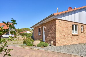 A single-story brick house with a red-tiled roof, a small front porch, and a gravel driveway. - Feriendorf Südstrand - Sun, beach & sauna - Lütt Strandhuus Pelzerhaken with (Neustadt in Holstein)