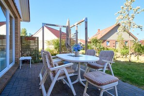 Une terrasse avec une table ronde et quatre chaises, une petite table et une structure de pergola en bois.