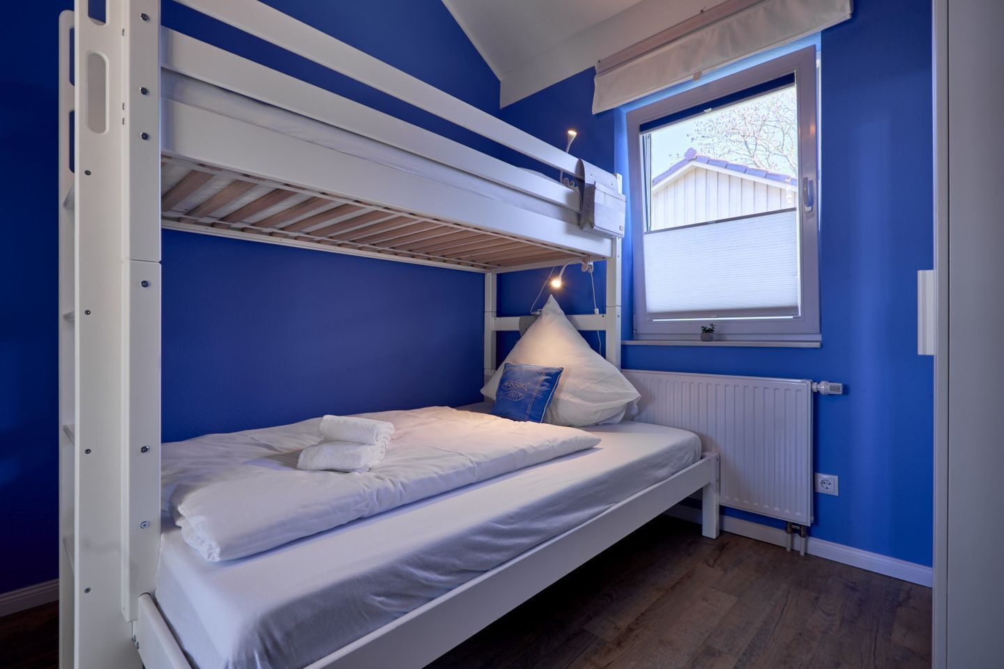 Une chambre avec un lit superposé, une fenêtre, du linge de lit blanc et un mur bleu.