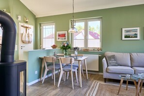 Ein gemütliches Wohnzimmer mit Sofa, einem Esstisch mit Stühlen, einer Küchenzeile mit Herd und einem großen Fenster.