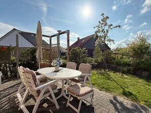 Une terrasse avec une table ronde et des chaises, entourée d’une clôture en bois et de verdure.