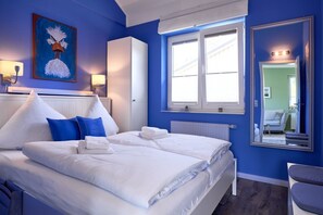Une chambre d’hôtel avec un lit, une fenêtre, un radiateur, un miroir et un tableau au mur.