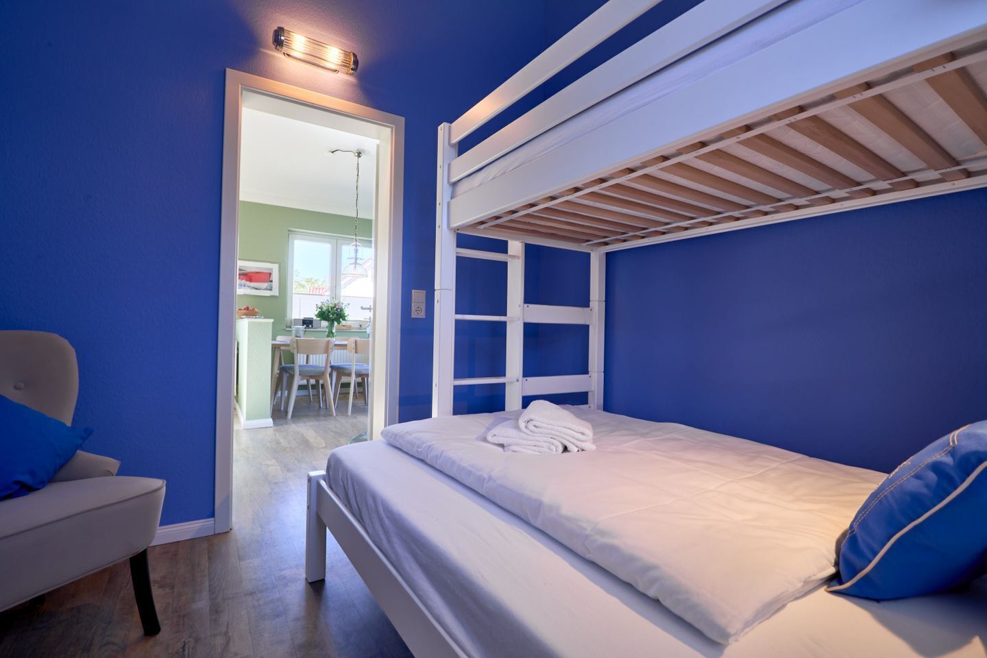 A room with a bunk bed, a chair, and a desk with chairs.