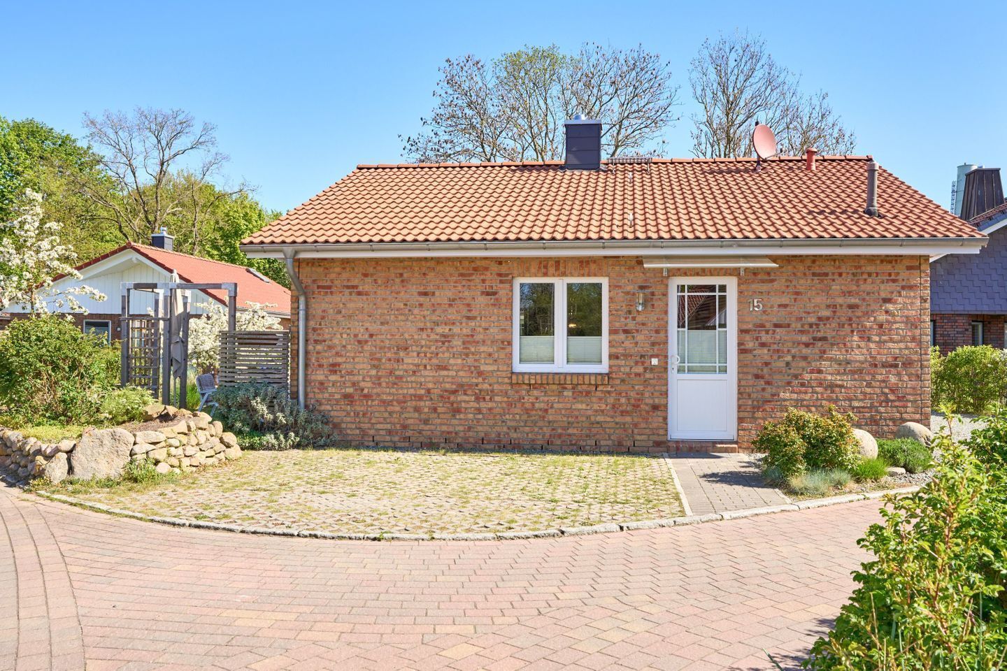 A small brick house with a tiled roof, a white door, and a small garden area.