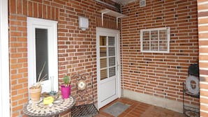Pieni patio, jossa on laatoitettu lattia, metallinen tuoli, ruukkukasveilla koristeltu pöytä ja valkoinen ovi.