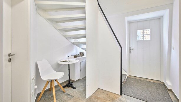 Una habitación con una silla blanca, una mesa redonda pequeña y una puerta que da a otra estancia.
