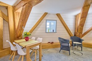 A room with a sloped ceiling, wooden beams, a dining table with chairs, a vase with flowers, and a window with a view. - fewo1846 - Nordwind - Vacation in a historic windmill with max. 2 persons (Flensburg)