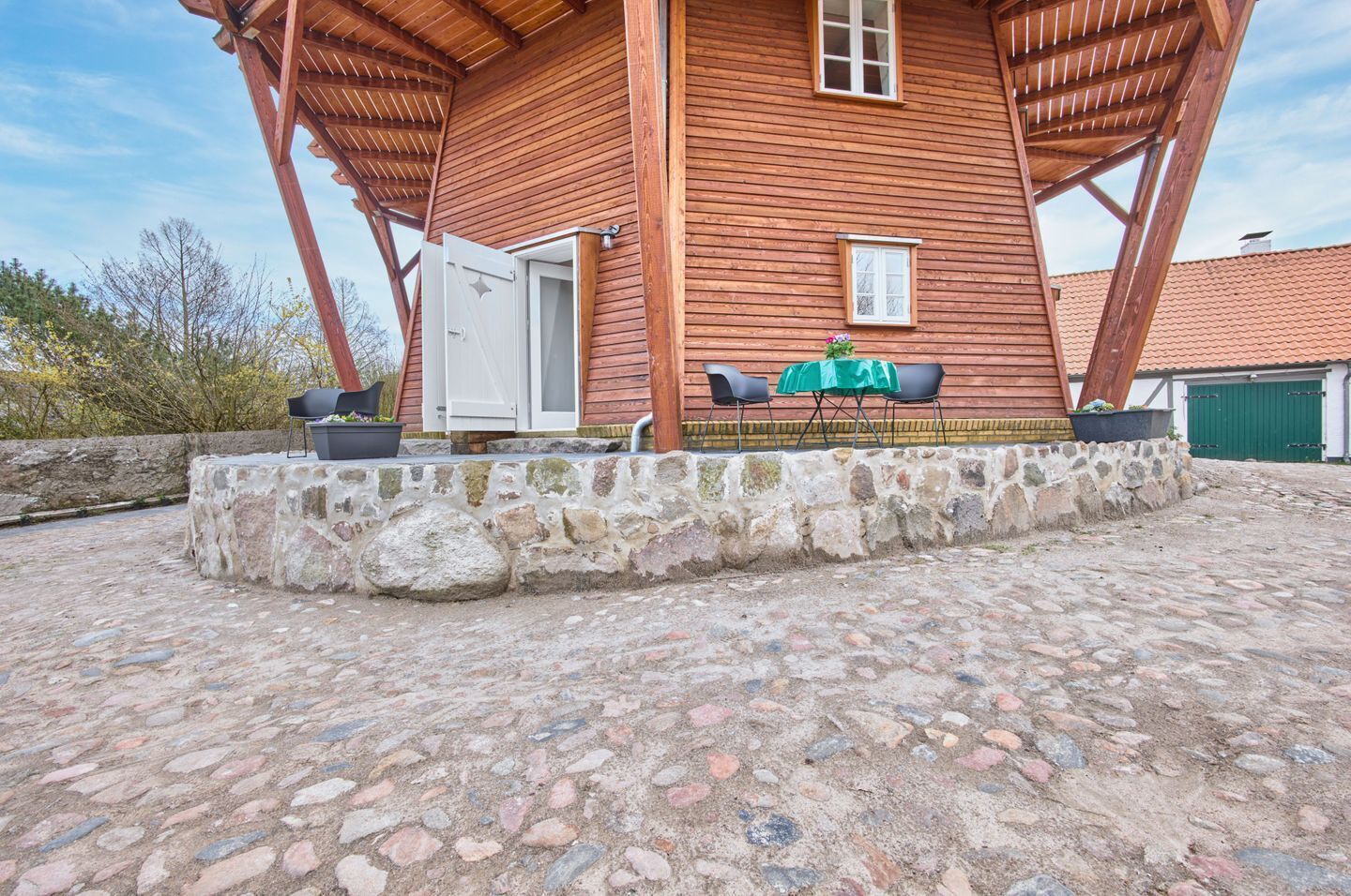 Ein Holzhaus mit Steinunterbau, einer Tür und einem kleinen Tisch mit Stühlen vor der Tür.