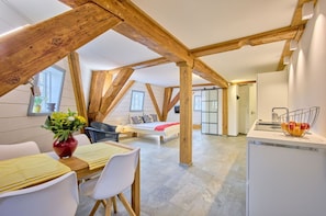 A loft-style room with exposed wooden beams, a dining area with a table and chairs, a bed with a view, and a kitchenette. - fewo1846 - Nordwind - Vacation in a historic windmill with max. 2 persons (Flensburg)