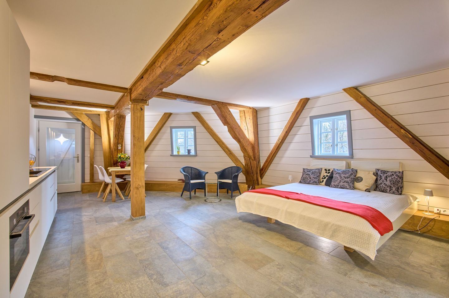 Ein Schlafzimmer mit einem großen Bett, Holzbalken, einem Schreibtisch und zwei Stühlen.