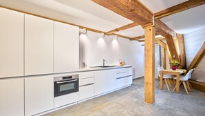 Una cocina moderna con armarios blancos, horno empotrado y comedor con mesa y sillas de madera.