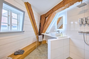 A bathroom with a wooden beam ceiling, a window, a sink, a mirror, and a shower. - fewo1846 - Nordwind - Vacation in a historic windmill with max. 2 persons (Flensburg)