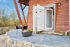 Ein Holzgebäude mit einer weißen Tür, einem schwarzen Stuhl und einem Blumentopf mit Blumen.