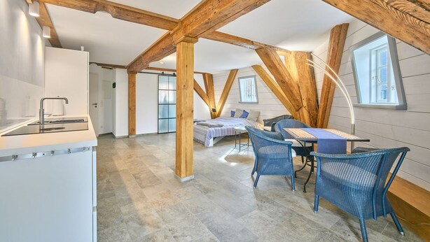 Une chambre spacieuse de style loft, dot ée d’un grand lit, d’un bureau et d’une chaise, de poutres en bois et d’une lucarne.