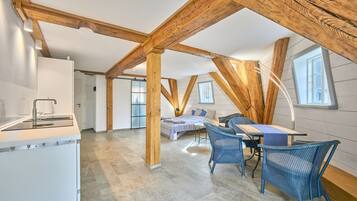 Ein geräumiges Schlafzimmer im Loft-Stil mit einem großen Bett, einem Schreibtisch und einem Sessel, Holzbalken und einem Oberlicht.