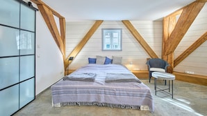 Une chambre à coucher avec un lit, une chaise, une fenêtre et des poutres en bois.