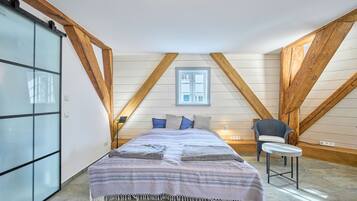 Ein Schlafzimmer mit Bett, Stuhl, Fenster und Holzbalken.