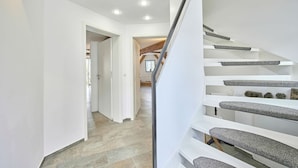 Un intérieur moderne avec un escalier, des murs blancs et un sol en pierre.