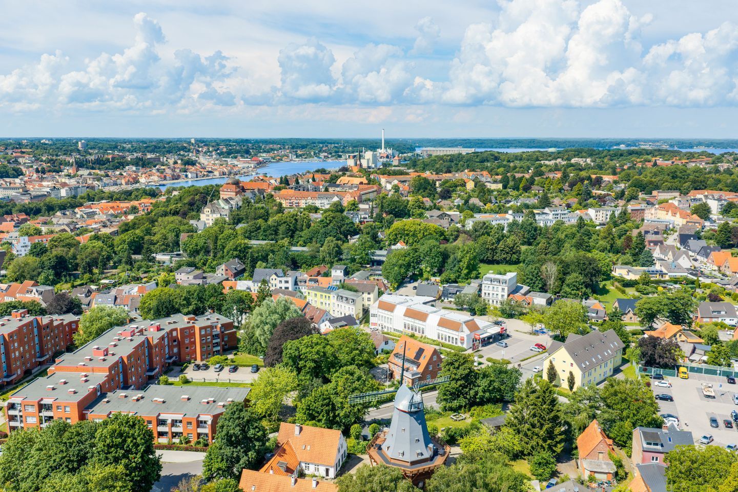 Luchtbeeld van een stadsgezicht met een combinatie van woon- en bedrijfsgebouwen, een opvallende kerk met een hoge punt en een groot wateroppervlak in de verte.