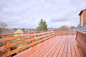 Eine Holzterrasse mit Geländer, mit Blick auf eine Wohngegend mit Häusern und Bäumen.