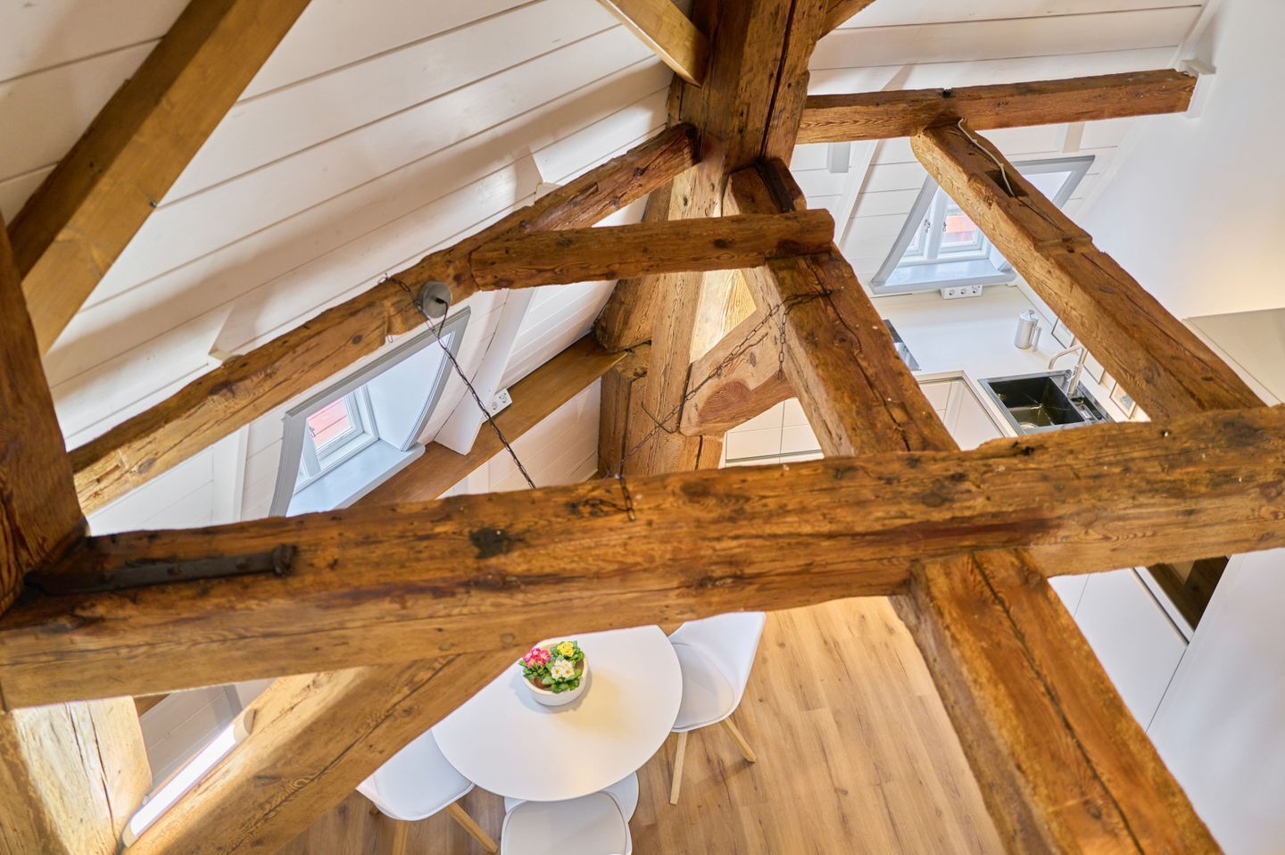 Ein Zimmer mit freiliegenden Holzbalken, weißen Wänden und einem weißen Tisch mit Stühlen.