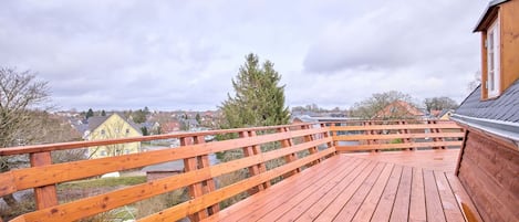 A wooden deck with a railing, overlooking a residential area with houses and trees.