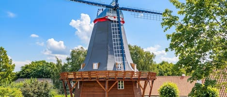 Un moulin à vent traditionnel, doté d’une structure en bois et d’un toit rouge, entouré de verdure et surplombant un ciel dégagé.