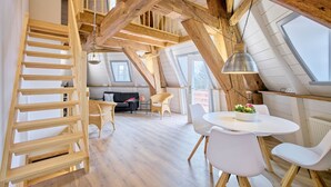 Avoin, loft-tyylinen huone, jossa on puinen portaikko, pyöreä ruokapöytä ja sohva.