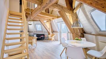 Ein Loft-Zimmer mit einer Holztreppe, einem runden Esstisch und einer Couch.