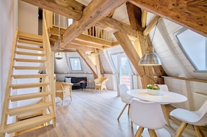 Ein Loft-Zimmer mit einer Holztreppe, einem runden Esstisch und einer Couch.