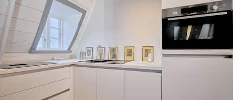 A modern kitchen with white cabinetry, a built-in oven, a window with a view, and framed artwork on the wall.