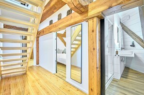 A room with wooden flooring, a staircase, a white wall, and a bathroom with a sink and mirror. - fewo1846 - Westwind - Vacation in a historic windmill with max. 4 persons (Flensburg)
