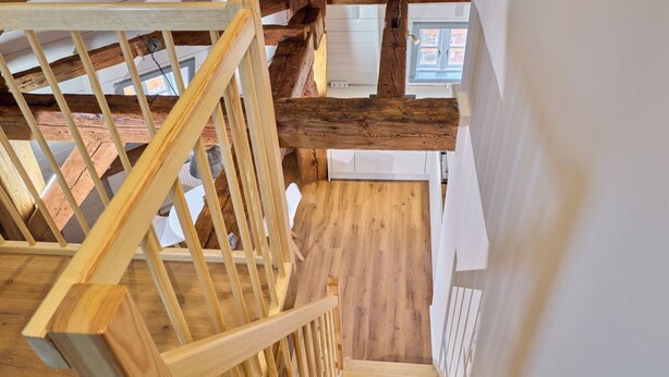 A wooden staircase with a railing, a wooden floor, and a white wall.