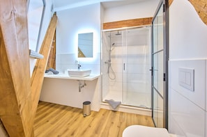 Ein modernes Badezimmer mit Holzboden, einem weißen Waschbecken, einer Duschkabine aus Glas und einem Spiegel mit Holzrahmen.