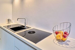 A modern kitchen with a black induction cooktop, a stainless steel sink, and a fruit bowl on the countertop. - fewo1846 - Westwind - Vacation in a historic windmill with max. 4 persons (Flensburg)