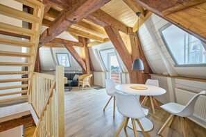 Ein Loft-Zimmer mit freiliegenden Holzbalken, einem runden Tisch mit Stühlen, einer Couch und einem Fenster.