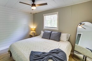 Ein Schlafzimmer mit Bett, Nachttisch mit Lampe, Deckenventilator, Fenster und Spiegel.