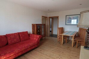 Ein Wohnzimmer mit rotem Sofa, Esstisch aus Holz, Stühlen und einem Schrank.