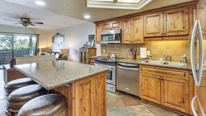 A kitchen with wooden cabinets, a granite countertop, stainless steel appliances, and a bar stool area. - Golf, Boat, Swim! Walkable Lake Havasu Getaway (Lake Havasu City)