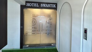 A modern hotel entrance with a frosted glass door, a digital elevator display, and a green artificial turf floor.