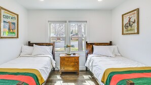 Ein Schlafzimmer mit zwei Betten, einem hölzernen Nachttisch, einem Fenster mit Blick und zwei gerahmten Postern an den Wänden.