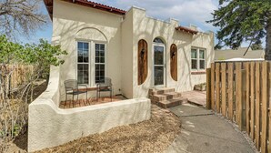 Ein Haus mit Putzfassade, Rundbogenfenstern, einer Holzterrasse und einem eingezäunten Garten.