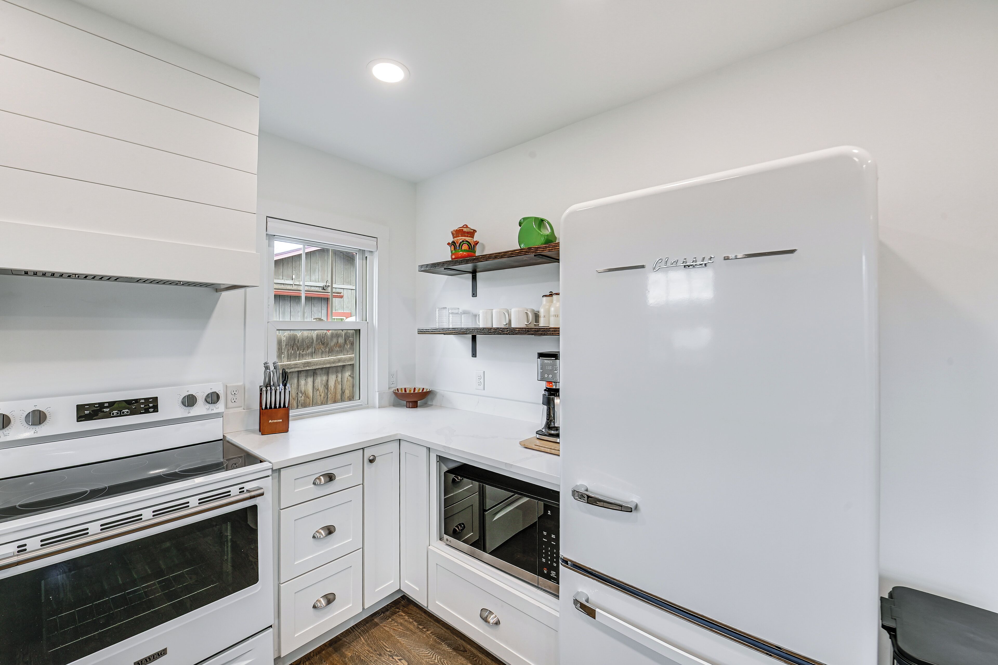 A kitchen with white cabinetry, a built-in oven, a refrigerator, and a window.