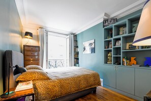 Ein Schlafzimmer mit einem Bett, einem Schminktisch, einer Lampe und einem Bücherregal.