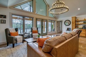 A spacious living area with a large sofa, armchairs, a coffee table, and a chandelier. - 'CopperTop Cabin' Waterfront White River Retreat (Norfork)