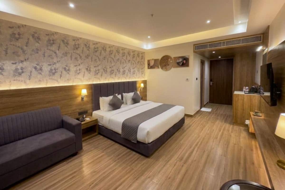 Una habitación de hotel moderna con una cama grande, un sofá, un televisor y piso de madera.