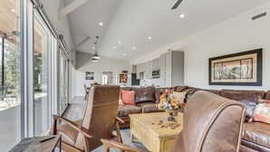 A spacious living area with leather sofas, a coffee table, and a large window offering a view of the outdoors. - Mtn & Creek Views! Harrisonburg Escape on 10 Acres (Harrisonburg)