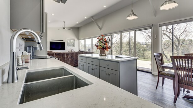 A modern kitchen with a large island, a dining area with a table and chairs, and a view through large windows. - Mtn & Creek Views! Harrisonburg Escape on 10 Acres (Harrisonburg)