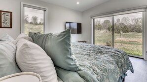 A bedroom with a bed, pillows, a television, and large windows with a view of the outdoors. - Mtn & Creek Views! Harrisonburg Escape on 10 Acres (Harrisonburg)