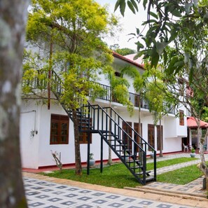 Un edificio blanco con techo rojo, escalera negra y un patio con baldosas.